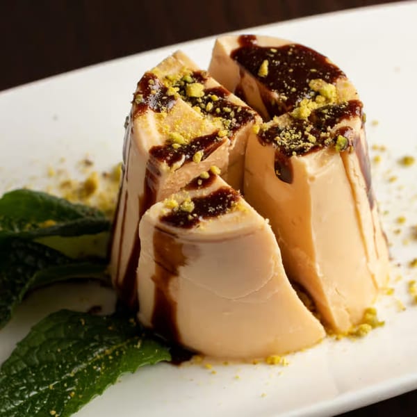 Indian dessert, a sliced round of light brown pudding drizzled with chocolate and sprinkled with pistachios.