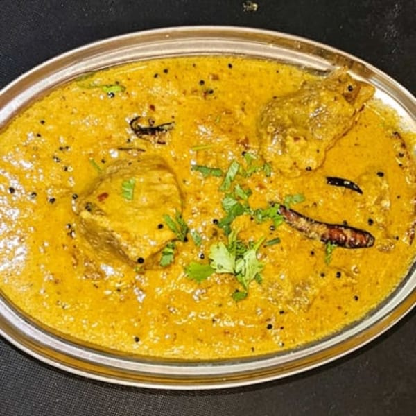 Indian chicken curry in a silver dish, garnished with cilantro and dried red chilies.