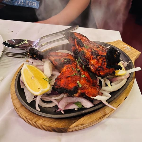 Two pieces of Tandoori Chicken on a sizzling platter with onions and lemon wedges.