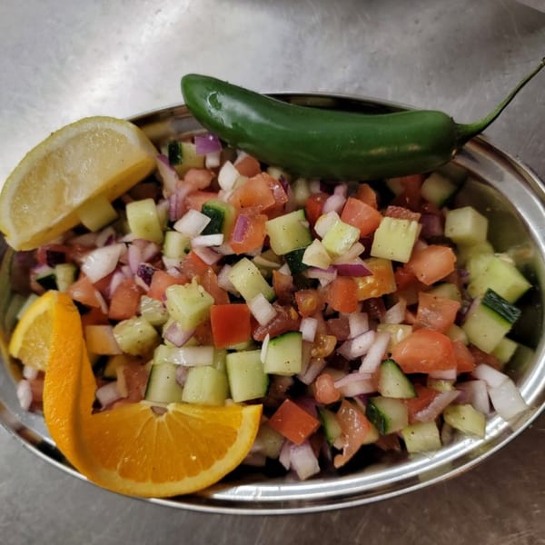 Diced cucumber, tomato, and onion salad, garnished with lemon, orange, and a green chili.