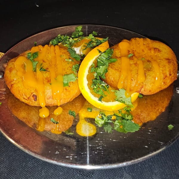 Two golden-brown Indian cutlets drizzled with orange sauce and garnished with cilantro and orange slices.